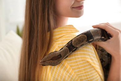 Photo of Young woman with boa constrictor at home, closeup. Exotic pet