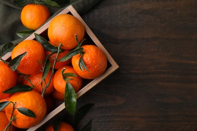 Fresh ripe tangerines with green leaves in crate on wooden table, top view. Space for text