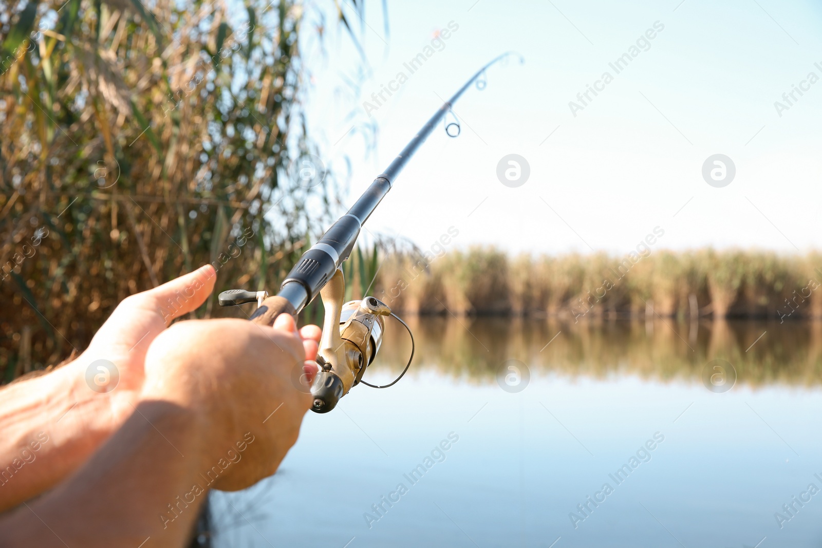 Photo of Man fishing alone at riverside on sunny day, closeup