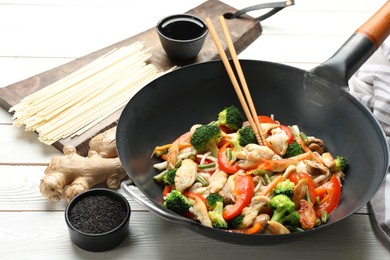Photo of Stir fried noodles with mushrooms, chicken and vegetables in wok on white wooden table