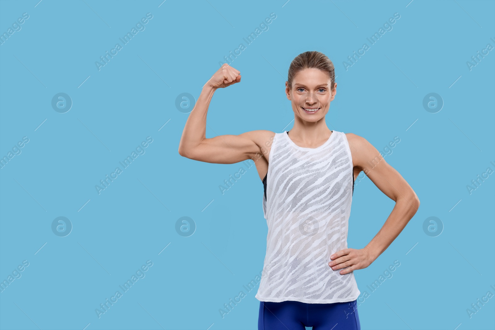 Photo of Portrait of sportswoman showing muscles on light blue background, space for text