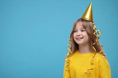 Photo of Happy little girl in party hat on light blue background. Space for text