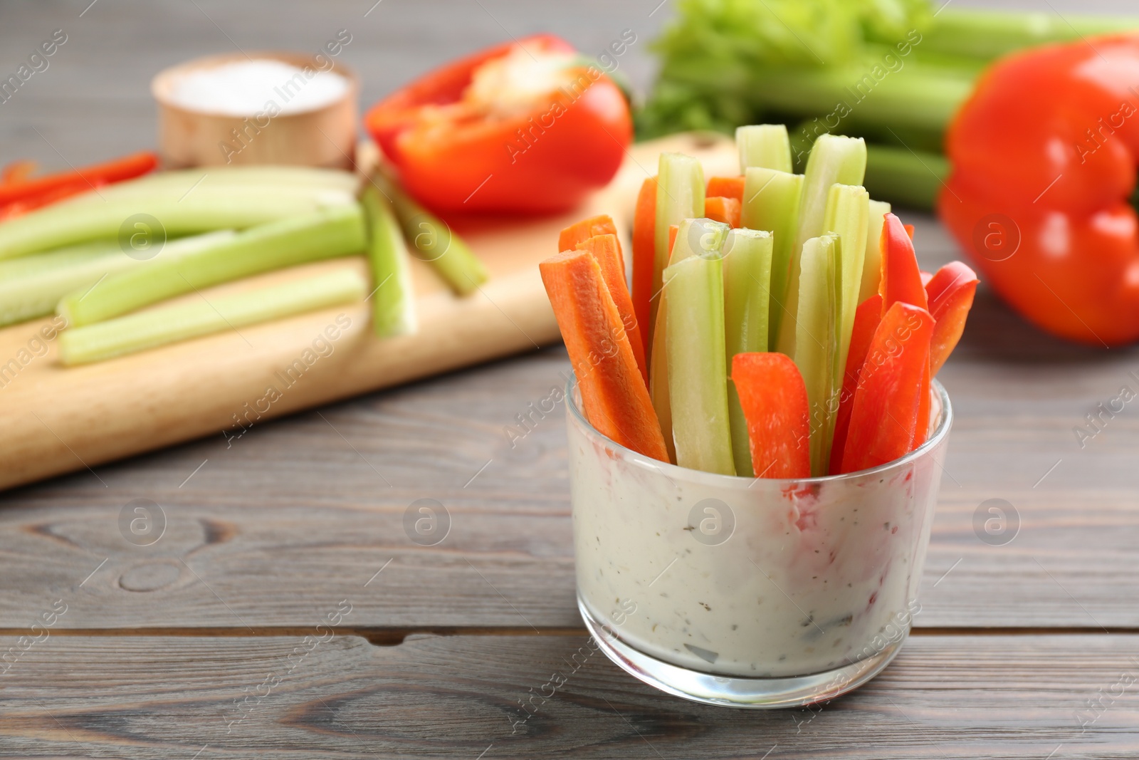 Photo of Celery and other vegetable sticks with dip sauce in glass bowl on wooden table. Space for text