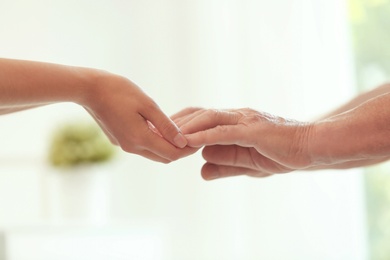 Photo of Young woman holding elderly man hands on blurred background, closeup. Help service