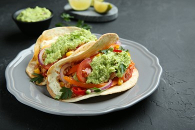 Photo of Delicious tacos with guacamole, meat and vegetables on black table, closeup