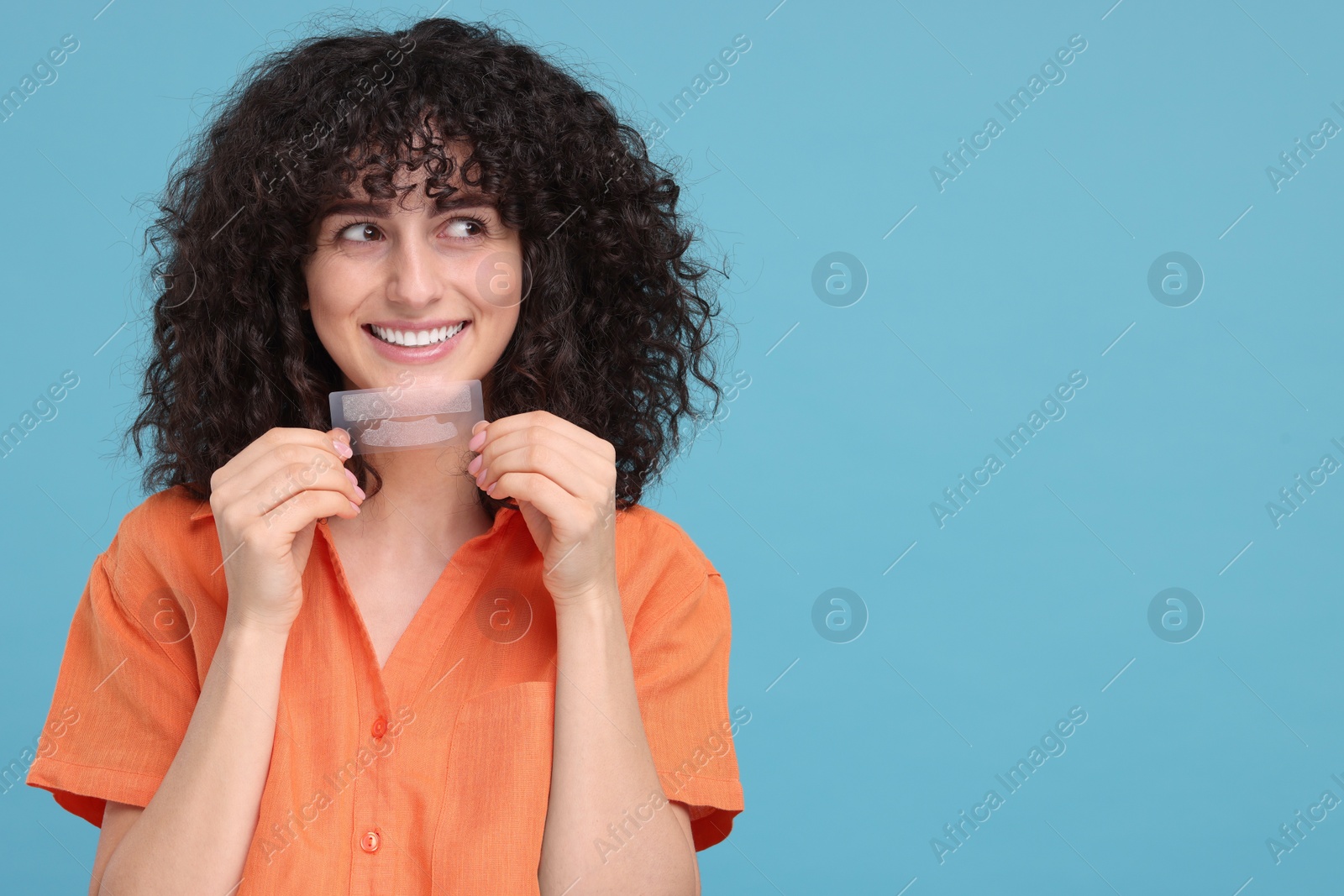 Photo of Young woman holding teeth whitening strips on light blue background, space for text