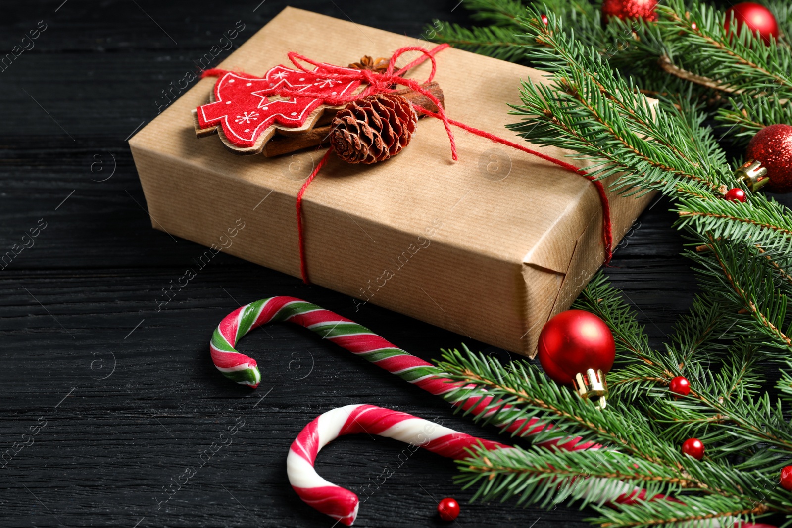 Photo of Gift box, candy canes, fir tree branches and Christmas decor on black wooden table