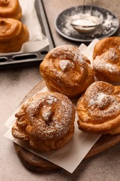 Photo of Many delicious profiteroles with powdered sugar on grey table, closeup