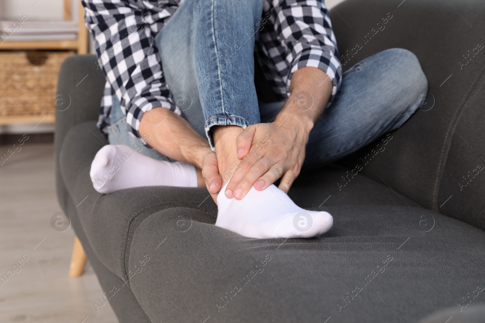 Photo of Man suffering from foot pain on sofa at home, closeup