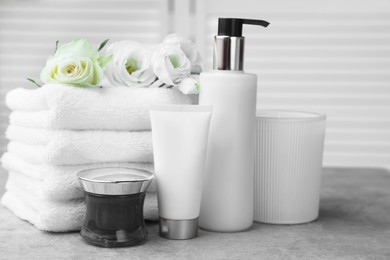 Photo of Towels, cosmetic products and flowers on grey table indoors