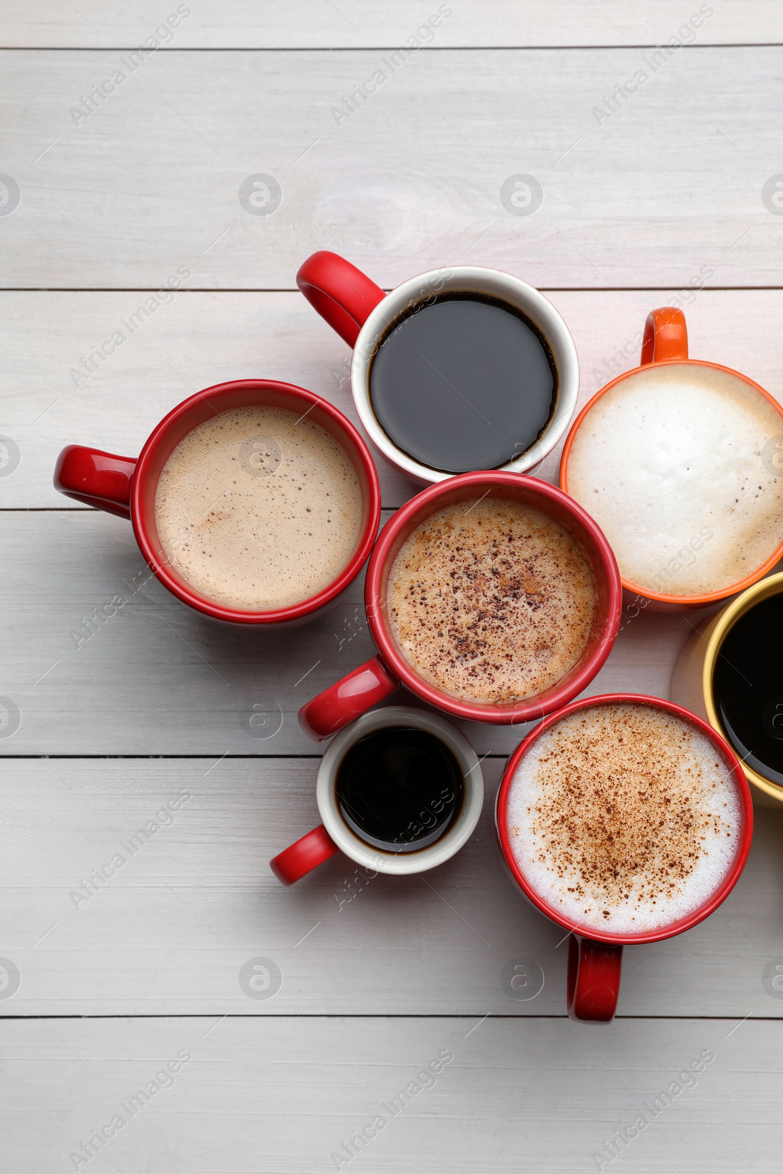Photo of Many different cups with aromatic hot coffee on white wooden table, flat lay