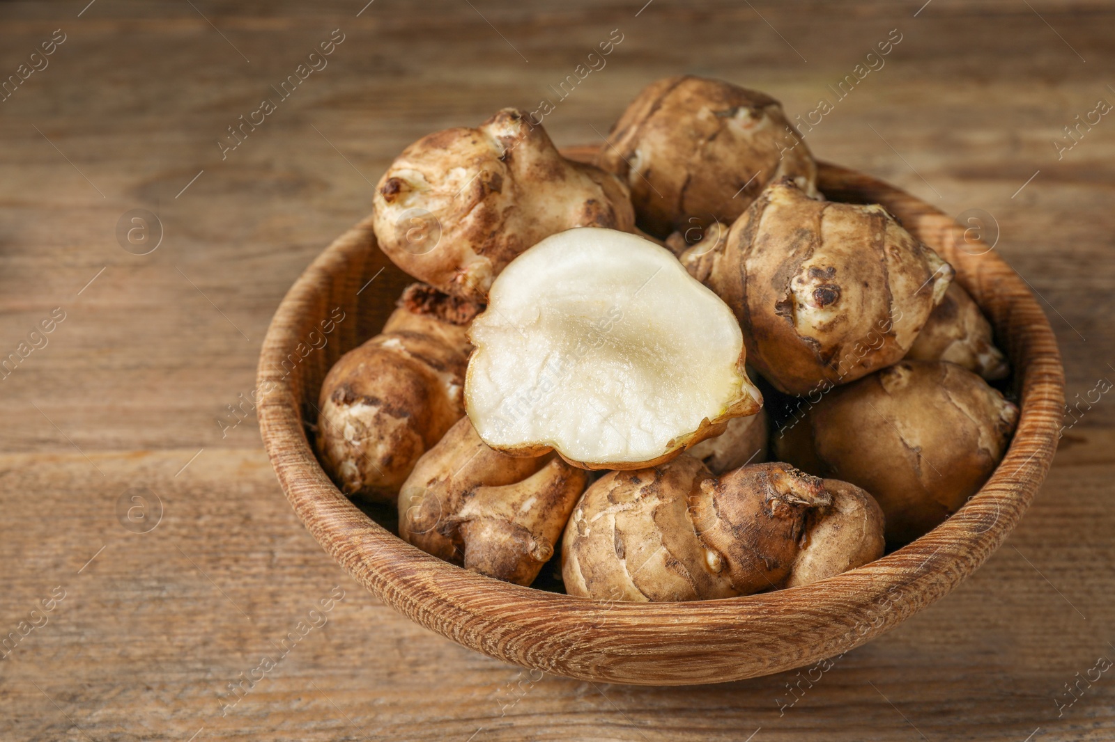 Photo of Bowl with whole and cut Jerusalem artichokes on wooden table, closeup