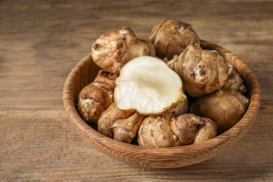 Photo of Bowl with whole and cut Jerusalem artichokes on wooden table, closeup