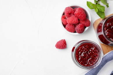 Photo of Delicious jam and fresh raspberries on white table, flat lay. Space for text