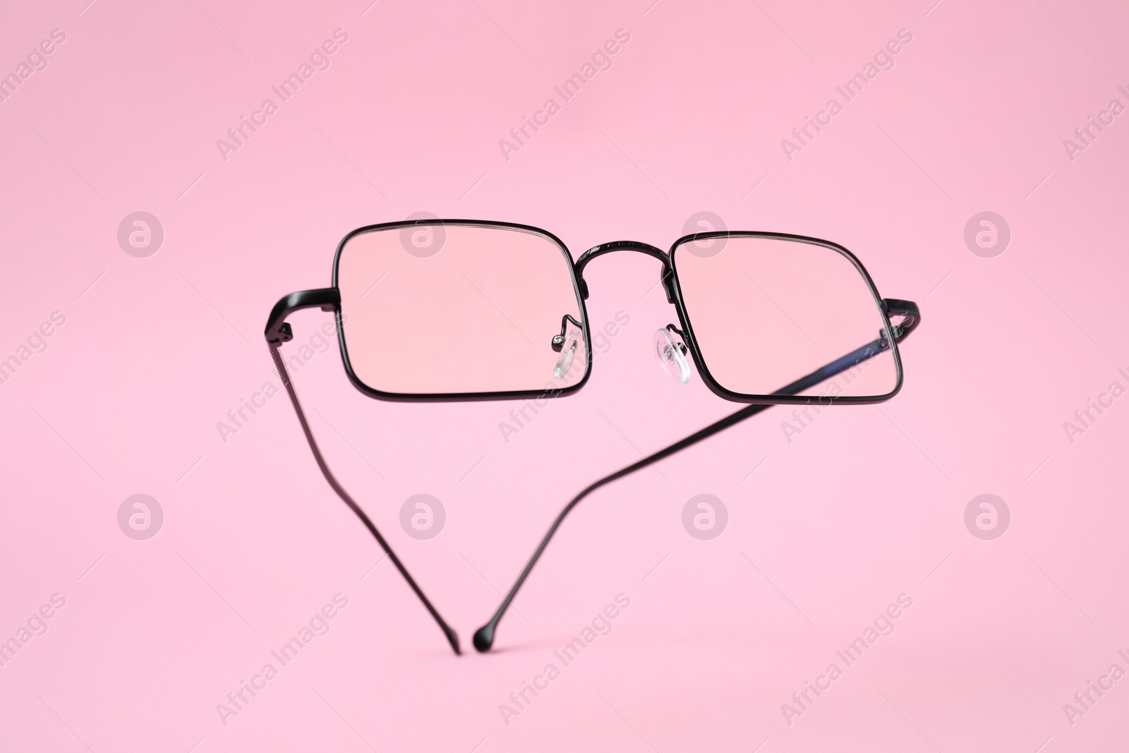 Photo of Stylish pair of glasses with black frame on pink background