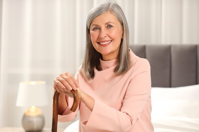 Mature woman with walking cane on bed at home