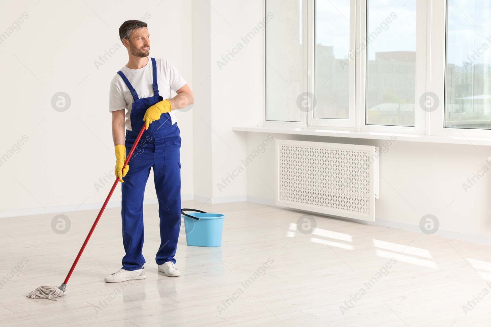 Photo of Man in uniform cleaning floor with mop indoors. Space for text