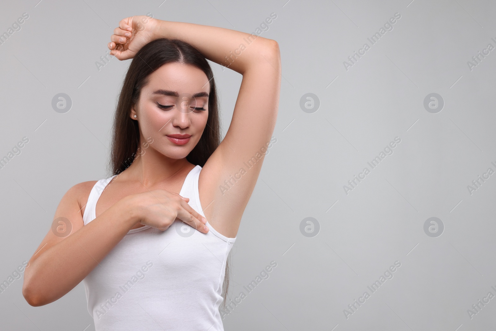 Photo of Beautiful young woman doing breast self-examination on light grey background, space for text