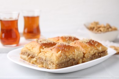 Photo of Eastern sweets. Pieces of tasty baklava and tea on white tiled table, closeup