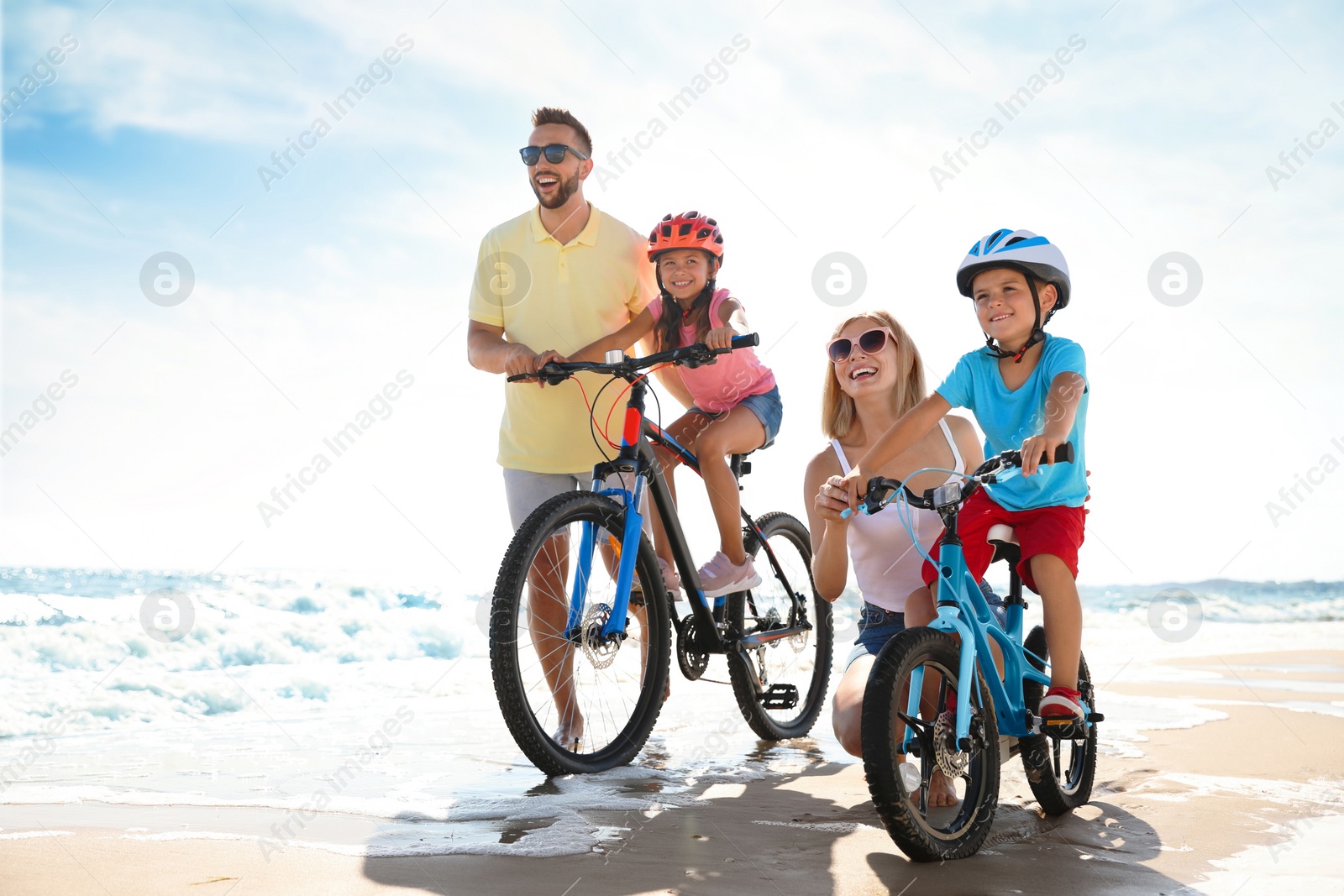 Photo of Happy parents teaching children to ride bicycles on sandy beach near sea