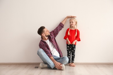 Photo of Young man measuring little girl's height indoors