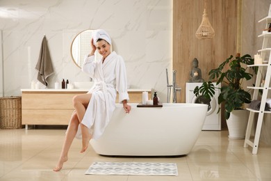 Photo of Beautiful young woman sitting on edge of tub in bathroom