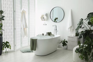 Photo of Stylish bathroom interior with modern tub, houseplants and beautiful decor. Home design