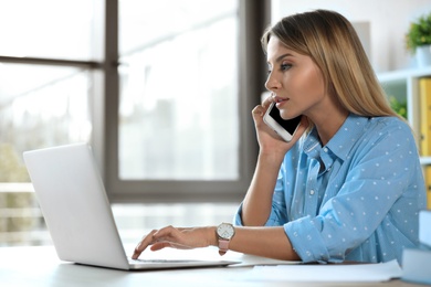 Photo of Female business trainer talking on phone while working with laptop in office