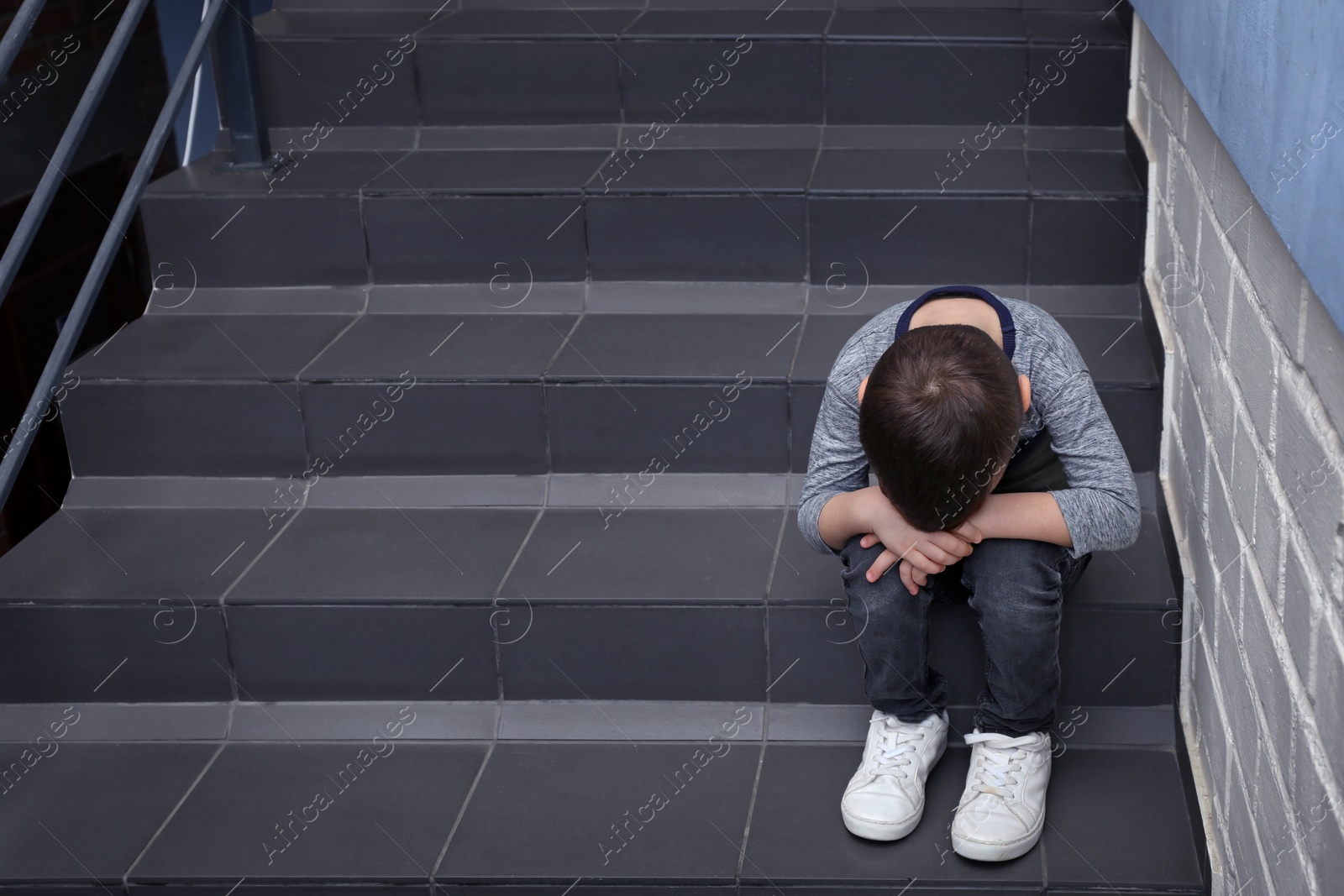 Photo of Sad little boy sitting on stairs indoors