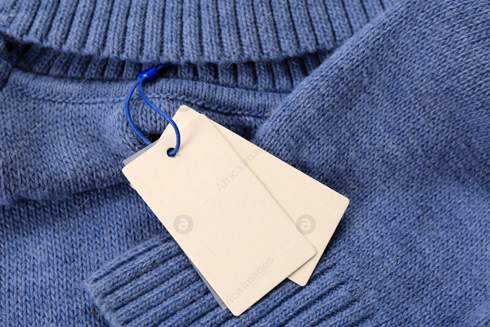 Photo of Blank white tags on blue knitted sweater. Space for text