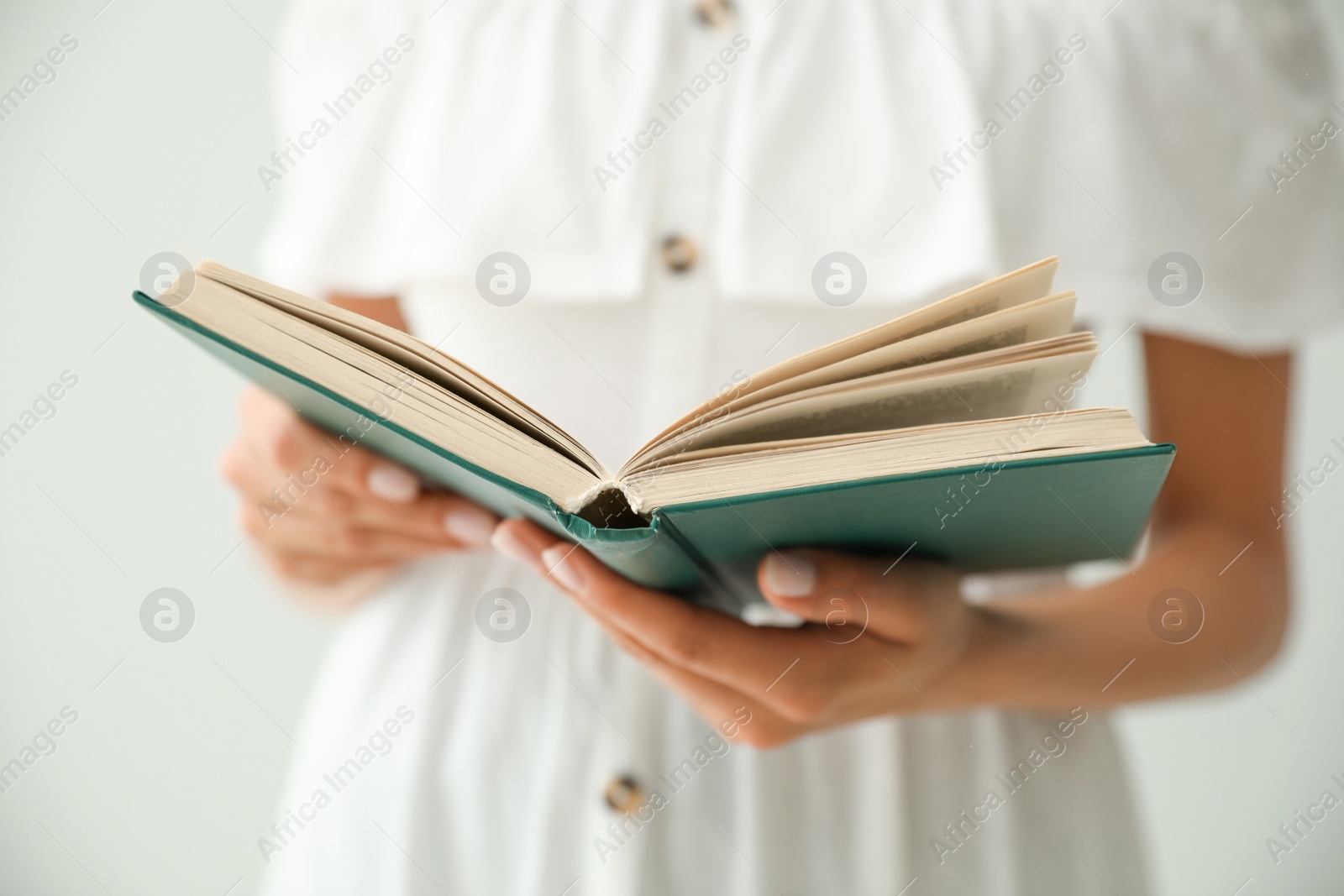 Photo of Young woman reading book on light grey background, closeup