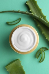 Photo of Jar of natural cream and aloe leaves on green background, flat lay