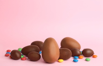 Photo of Sweet chocolate eggs and bright candies on pink background. Space for text