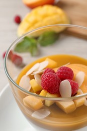 Photo of Delicious panna cotta with mango coulis, fresh fruit pieces and almond flakes in bowl, closeup