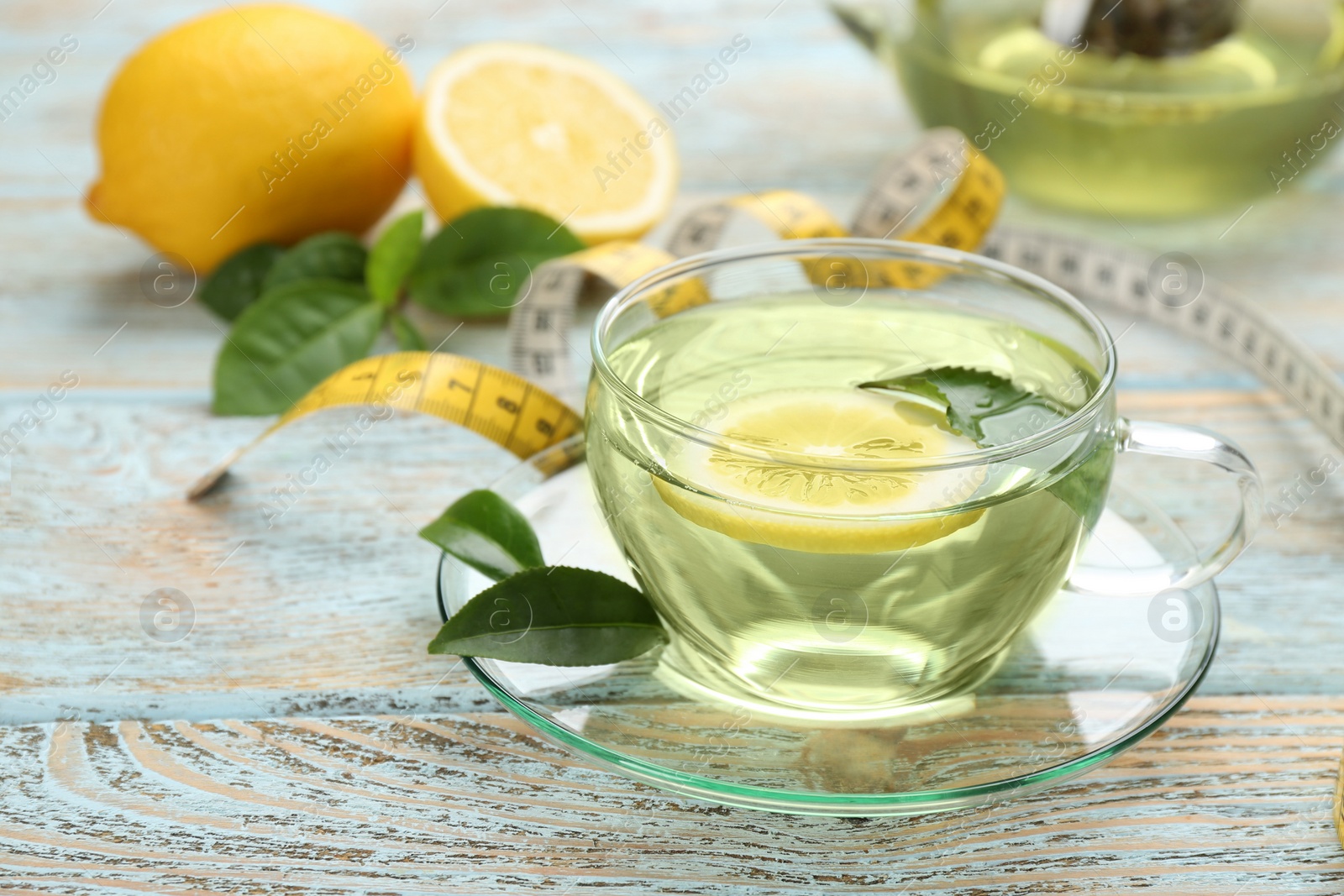 Photo of Glass cup of diet herbal tea with green leaves and lemon on wooden table