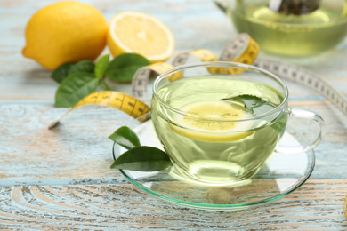 Photo of Glass cup of diet herbal tea with green leaves and lemon on wooden table