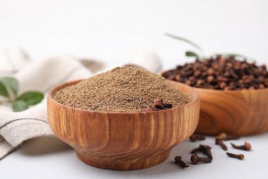 Photo of Aromatic clove powder and dried buds in bowls on white table, closeup