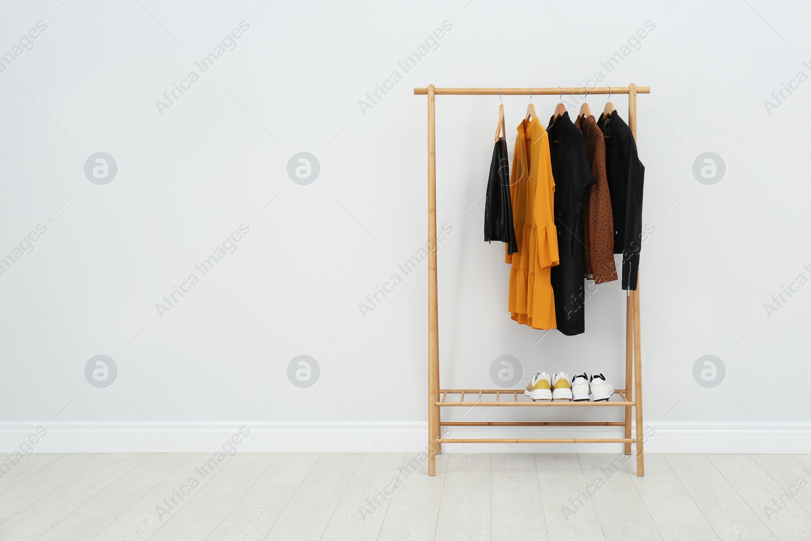 Photo of Wooden rack with stylish clothes in room. Space for text