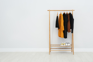 Photo of Wooden rack with stylish clothes in room. Space for text