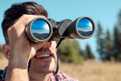 Image of Man looking through binoculars outdoors on sunny day. Mountain landscape reflecting in lenses