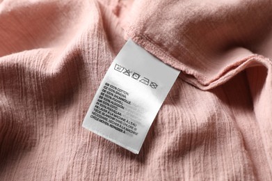 Clothing label on beautiful pink garment, closeup view