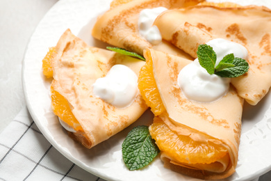 Photo of Delicious thin pancakes with oranges and cream on light table, closeup