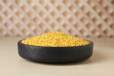 Bowl of uncooked bulgur on wooden table, closeup view