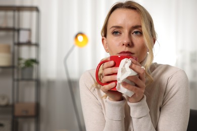 Photo of Sick woman with tissue and cup of drink at home. Cold symptoms