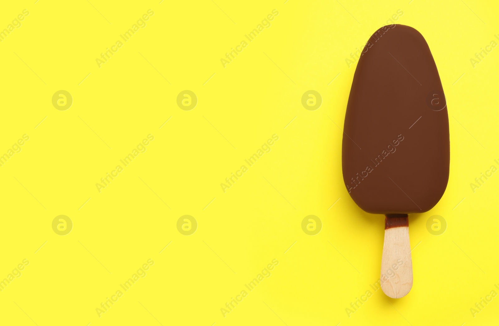 Photo of Ice cream glazed in chocolate on yellow background, top view. Space for text
