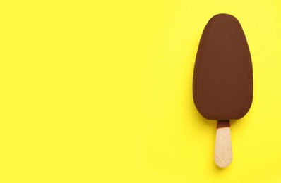 Photo of Ice cream glazed in chocolate on yellow background, top view. Space for text