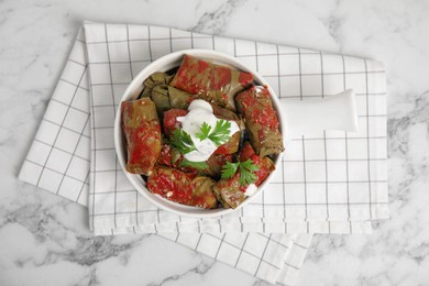 Photo of Delicious stuffed grape leaves with sour cream and tomato sauce on white marble table, top view