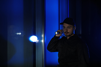 Male security guard with flashlight in dark corridor