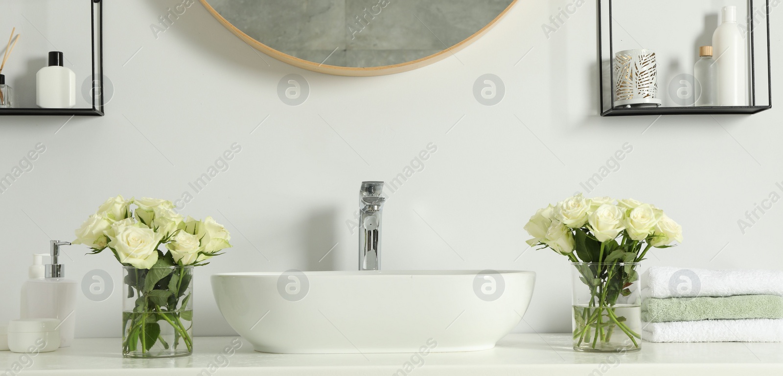 Photo of White sink between beautiful roses and toiletries in bathroom