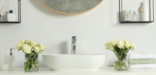 Photo of White sink between beautiful roses and toiletries in bathroom